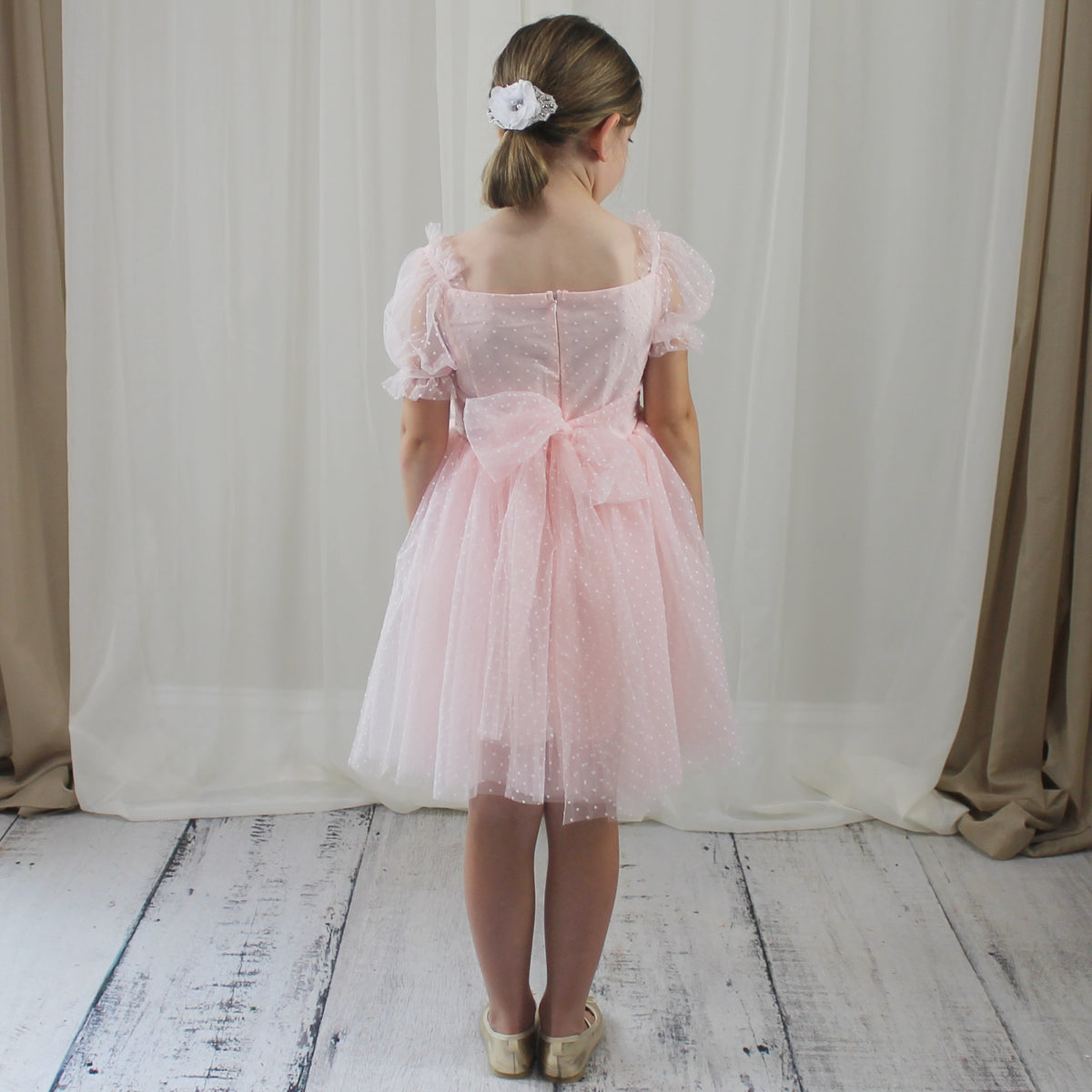 Light pink girls party dress featuring delicate Swiss dot tulle, short puff sleeves and a soft, flowing knee-length skirt.